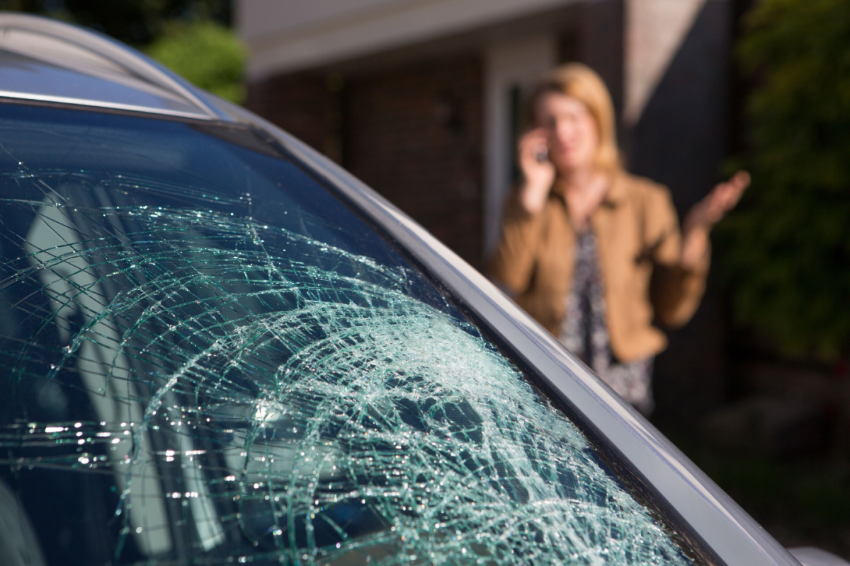 Shattered car windshield with driver in the background on the phone