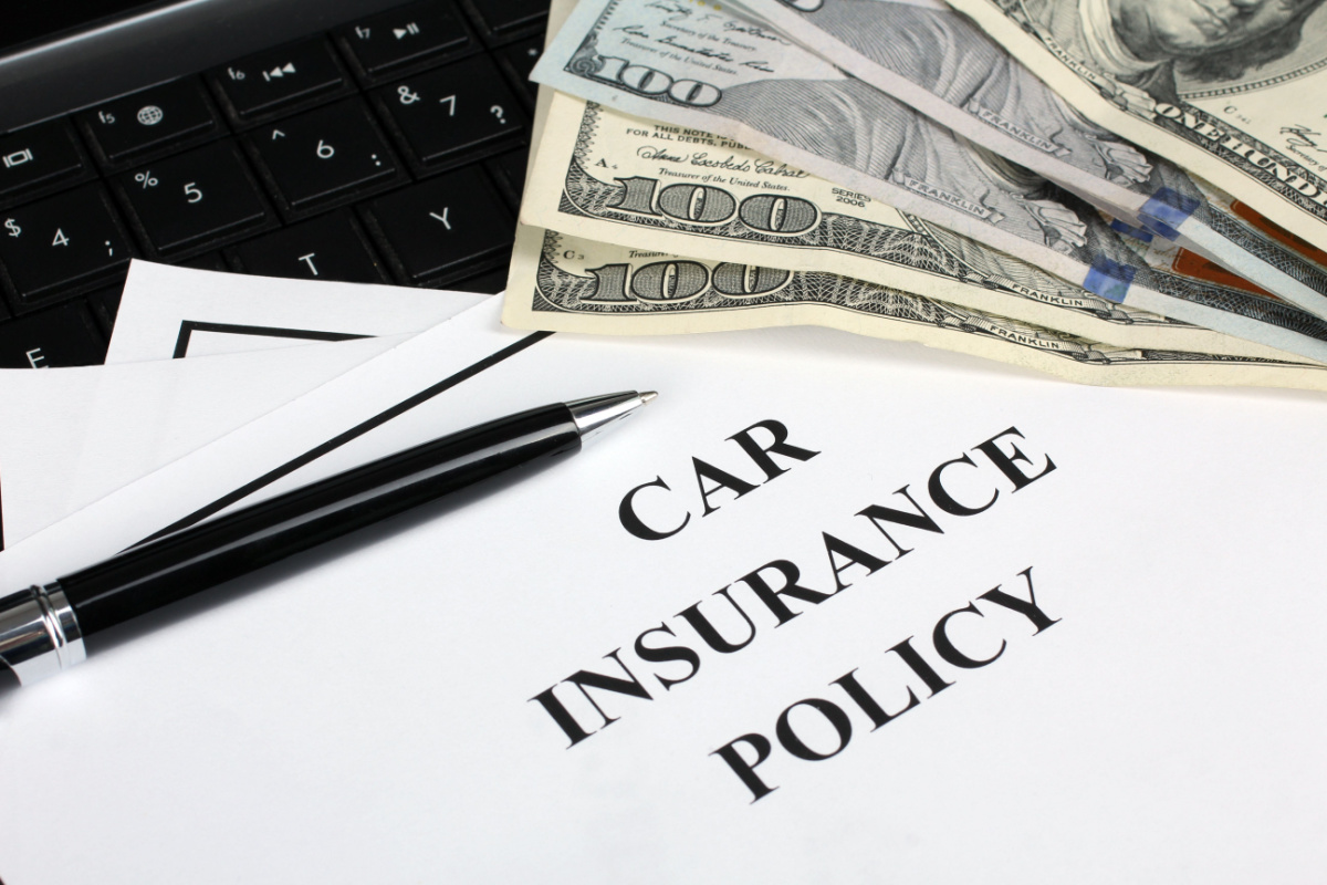 Close up on car insurance policy paperwork and $100 bills